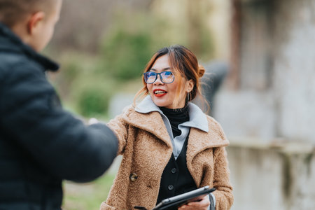 Friendly outdoor business meeting: woman in tan coat shakes hands with partner while smilingの写真素材