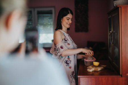 Smiling woman juicing a lemon in a home kitchen while someone photographs herの写真素材
