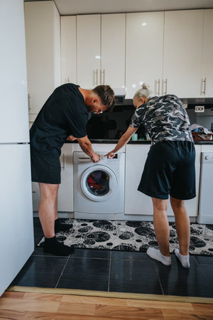Couple doing laundry together at home with a front-loading washing machine in the kitchenの写真素材