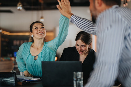Happy colleagues celebrate success with a high five during business collaboration in a modern office...