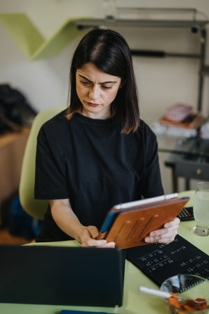 Women working on tablet and laptop in home office concentrating on documents and remote study