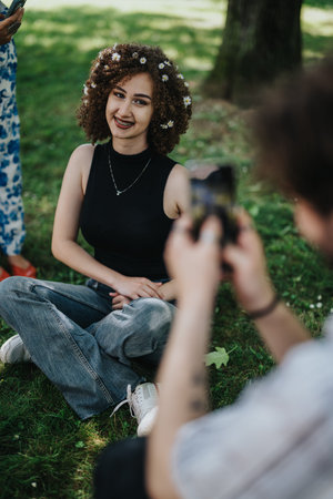 Young woman with a flower crown relaxing in the park while friends take photos, casual outdoor...