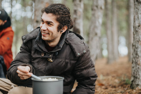 Smiling man camping in a forest cooking outdoors with friends on a cold day