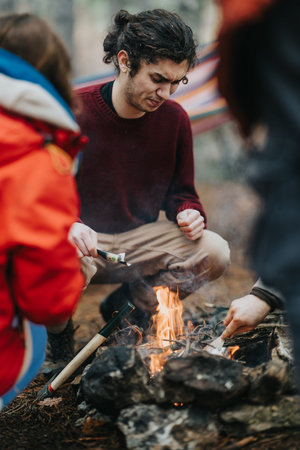 Friends gathered around a campfire while camping in the mountain forest on a cool day