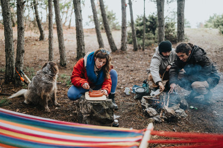 Friends cooking over campfire in mountain forest while dog watches during outdoor trip