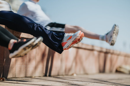 Sportspeople resting on a low wall after outdoor running training session with colorful running shoes