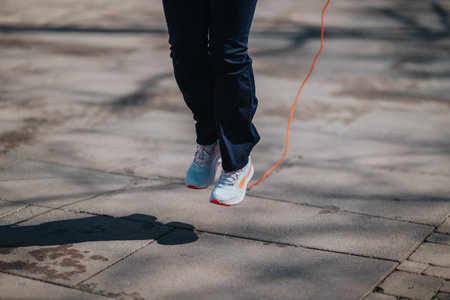 Person jumping rope outdoors in athletic shoes on paved path for fitness workout