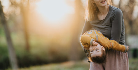 Mom playing with toddler upside down outdoors at golden hour in park