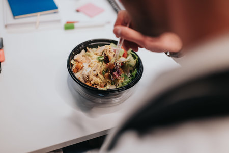 Business professional eating a takeaway salad at a white office desk during a quick lunch break