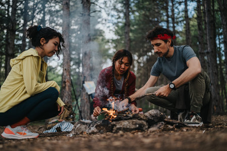 Three friends camping in a forest making a small campfire and preparing a fire together