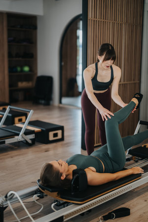 Female pilates instructor guiding client through reformer workout in modern fitness studio