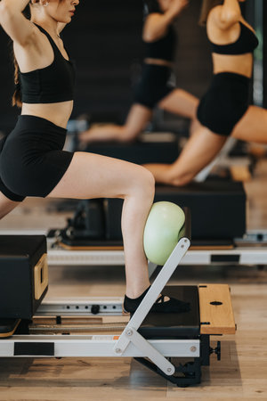 Young women doing pilates reformer lunges with stability ball in fitness studio class