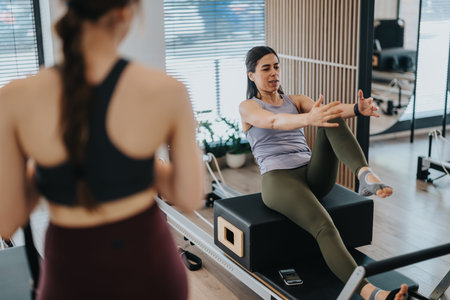 Woman performing reformer Pilates workout with trainer in a modern studio