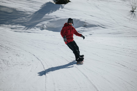 Male snowboarder in a red jacket carving down a sunlit snowy mountain slope
