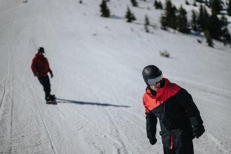 Two snowboarders riding down a sunny groomed slope at a snowy mountain resort
