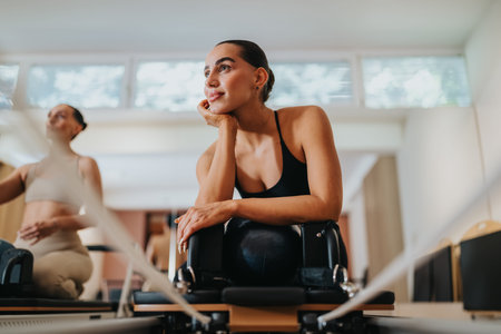 Young woman resting on a reformer machine during a pilates workout in a bright studio