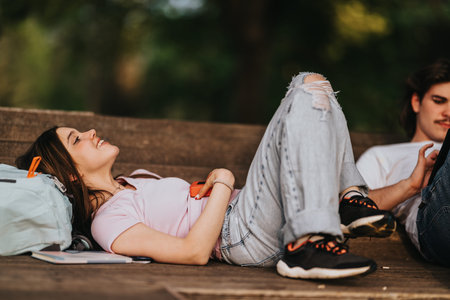 Teenage student relaxing on a park bench with backpack and phone in casual clothes