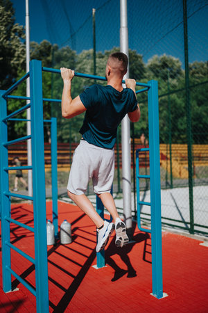Young man doing pull-ups at an outdoor gym on a sunny day for fitness workout