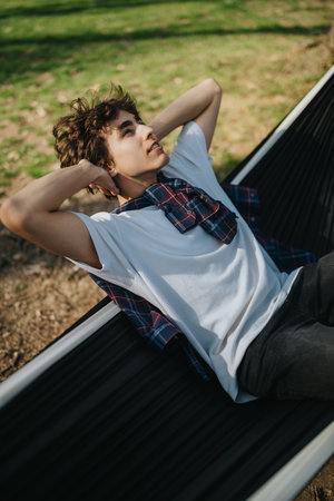 Young man relaxing in a hammock outdoors on a sunny day in a park wearing casual clothes