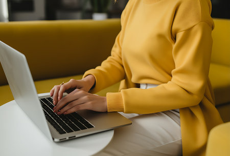 Cropped view of woman in yellow hoodie using laptop at homeの素材