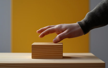 Wooden cube with human hand on table in front of orange backgroundの素材
