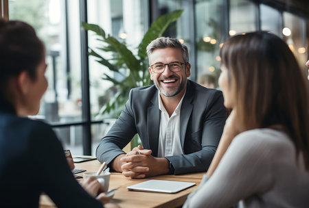 Smiling mature businessman sitting at table with colleagues during meeting in officeの素材