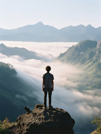 Man standing on the edge of a cliff looking at the misty valleyの素材