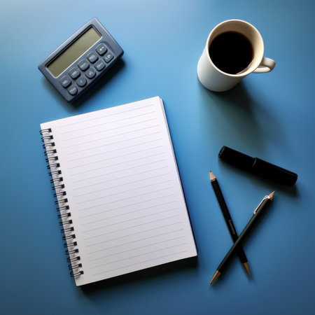 Notebook with pen, calculator and cup of coffee on blue backgroundの素材