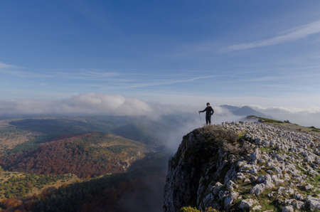 mountaineer on the summit with autumn forest and clouds at his feetの写真素材