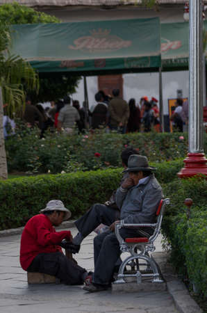Caraz, Peru, July 19, 2010: traditional shoe shiner cleaning shoes for men sitting on bench and market in the backgroundのeditorial素材