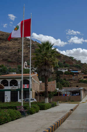 peruvian flag hoisted on mast in street surrounded by houses in andean town in peruの写真素材