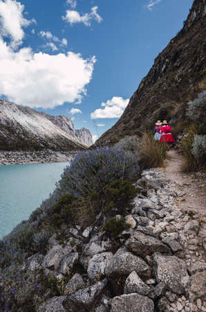 Ancash, Peru, July 29, 2014: two peruvian women in typical dress walking along a stone path in the turquoise lagoon of paron in the andesのeditorial素材