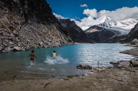 Ancash, Peru, July 29, 2014: dip bath of woman and man in frozen water of turquoise glacier lagoon with high mountain peak snowy of the andes in the backgroundのeditorial素材