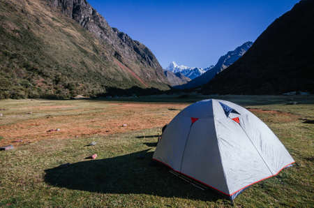gray camping tent with high snowy mountains in the background, on the trekking of the quebrada santa cruz in peruの写真素材