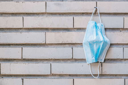 Surgical mask hanging on a nail disinfecting on a vintage brick wall, horizontal