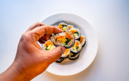 <p>Hands holding sushi roll on white plate, japanese food</p>の写真素材