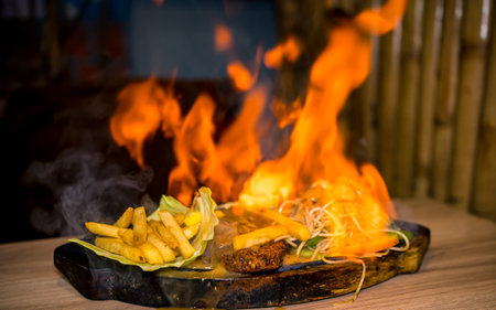 Grilled sizzler with french fries and vegetables on wooden tableの写真素材