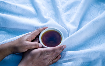 Hands holding a cup of tea on the bed, stock photo