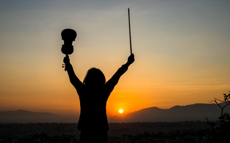Silhouette of a woman with a violin on sunset background.の写真素材