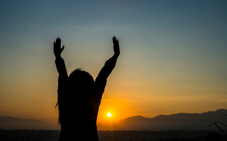 Silhouette of a woman with hands raised up in the sunsetの写真素材