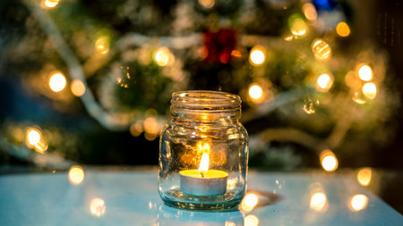 Candle in a glass jar on the background of the Christmas treeの写真素材