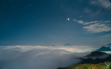 Fog in the mountains at night with starry sky and moonの写真素材