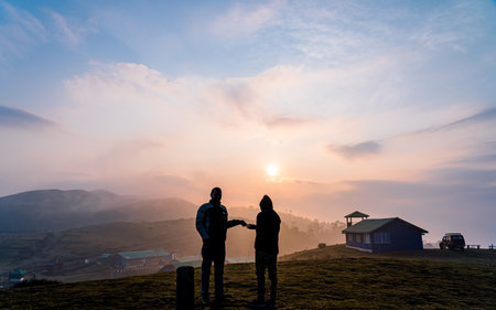 Silhouette of a man and woman standing on the top of the mountain and looking at the sunset
