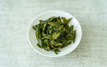Green tea leaves in white bowl on white tablecloth with copy space.