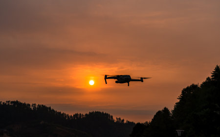Silhouette of drone flying in the orange sunset sky over the mountains