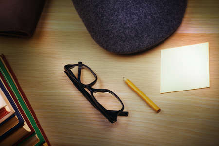 Books, hat,pencil, paper and reading glasses on a wooden table