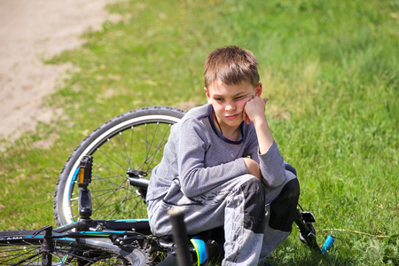 An upset boy sitting on a broken bike.の写真素材