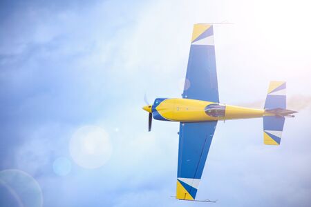 A small sport plane flying in the sky. A sun flare in the corner. Color of the plane is bluÑand yellow. a pilot can be seen through cabin's bulb.の写真素材