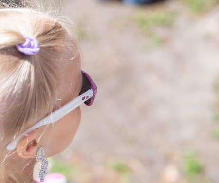 Little cute blond girl in a sunglasses looks somewhere. There is a heart on a sunglasses.の写真素材