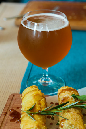 Crespelle and sprig of rosemary on a wooden desk. A glass of amber beer on the backgroundの写真素材
